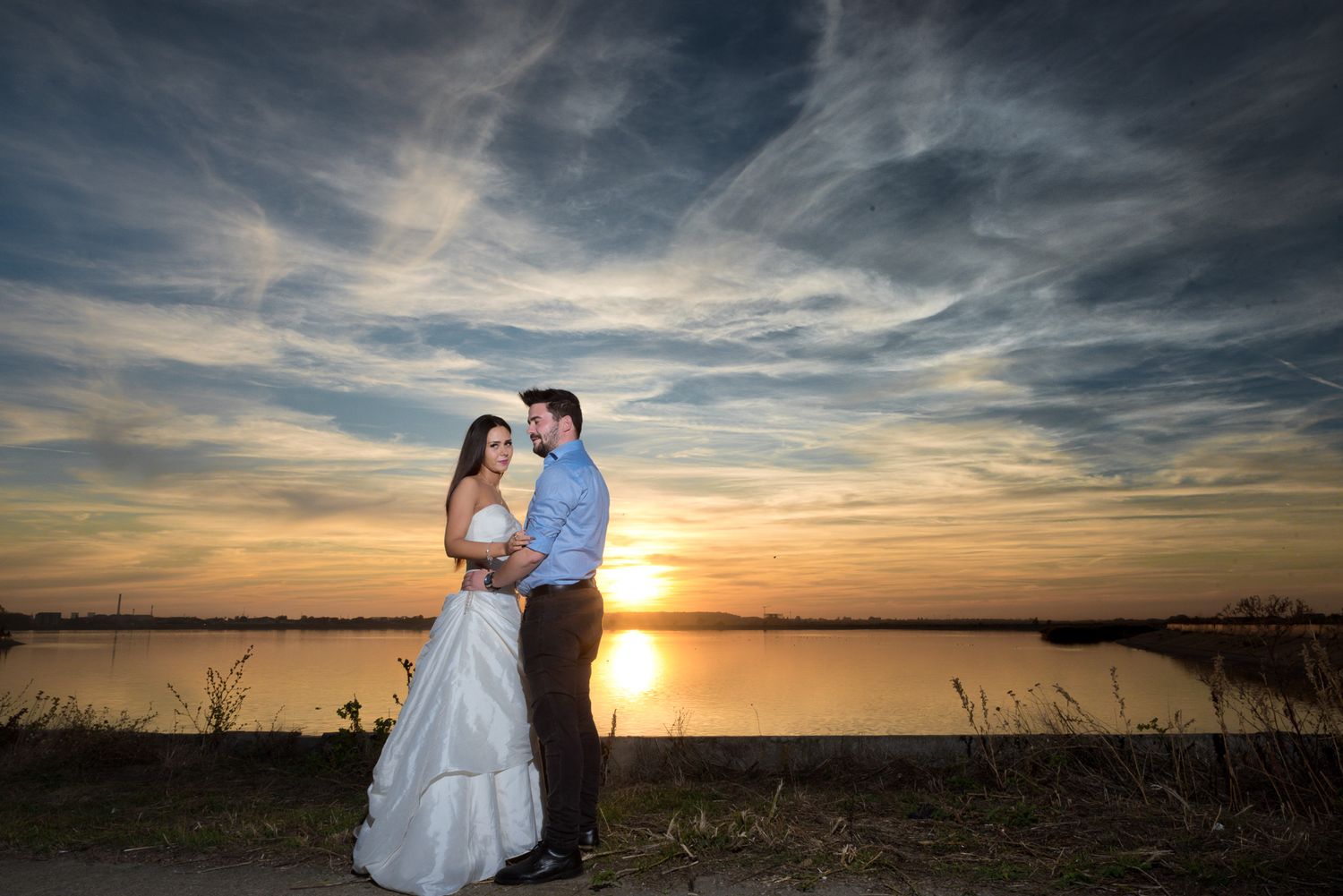 Romantic sunset wedding photos with dramatic clouds over a lake.