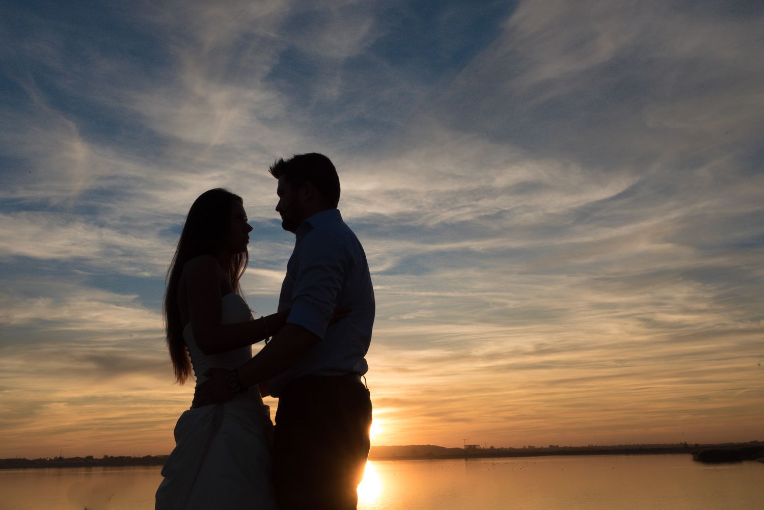 Silhouettes of a couple against a vibrant sunset sky over calm waters.
