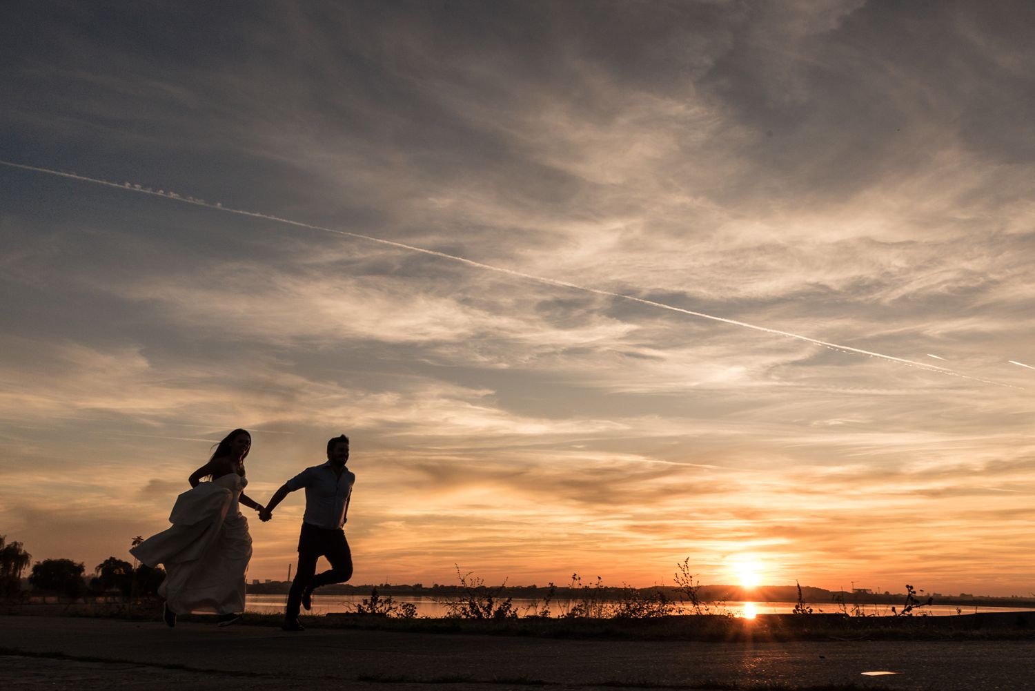 Wedding couple silhouetted against a dramatic orange sunset over a serene lake.