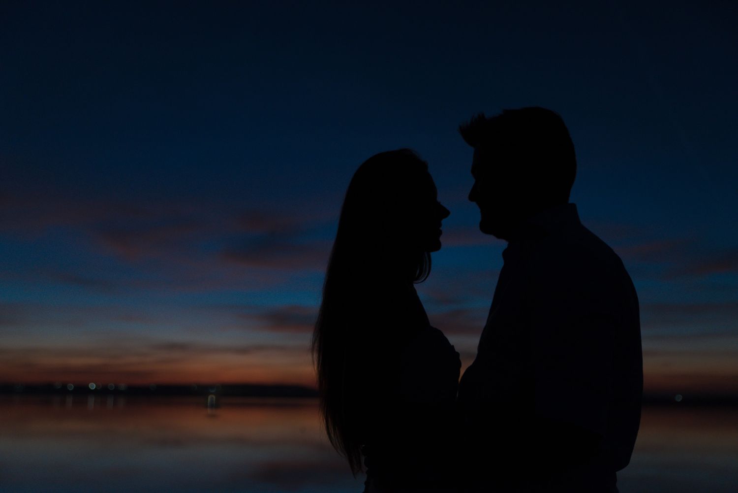 Silhouettes of a couple embracing during blue hour with a colorful sunset sky.