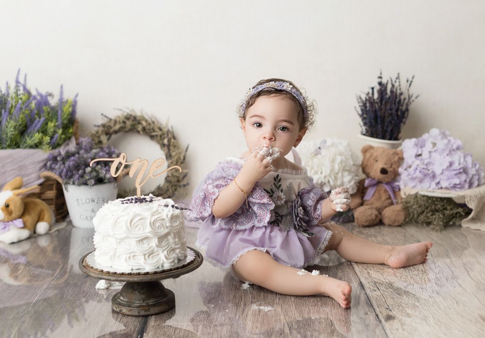 Rustic cake smash setup with lavender, teddy bears and white cake on wooden floor.