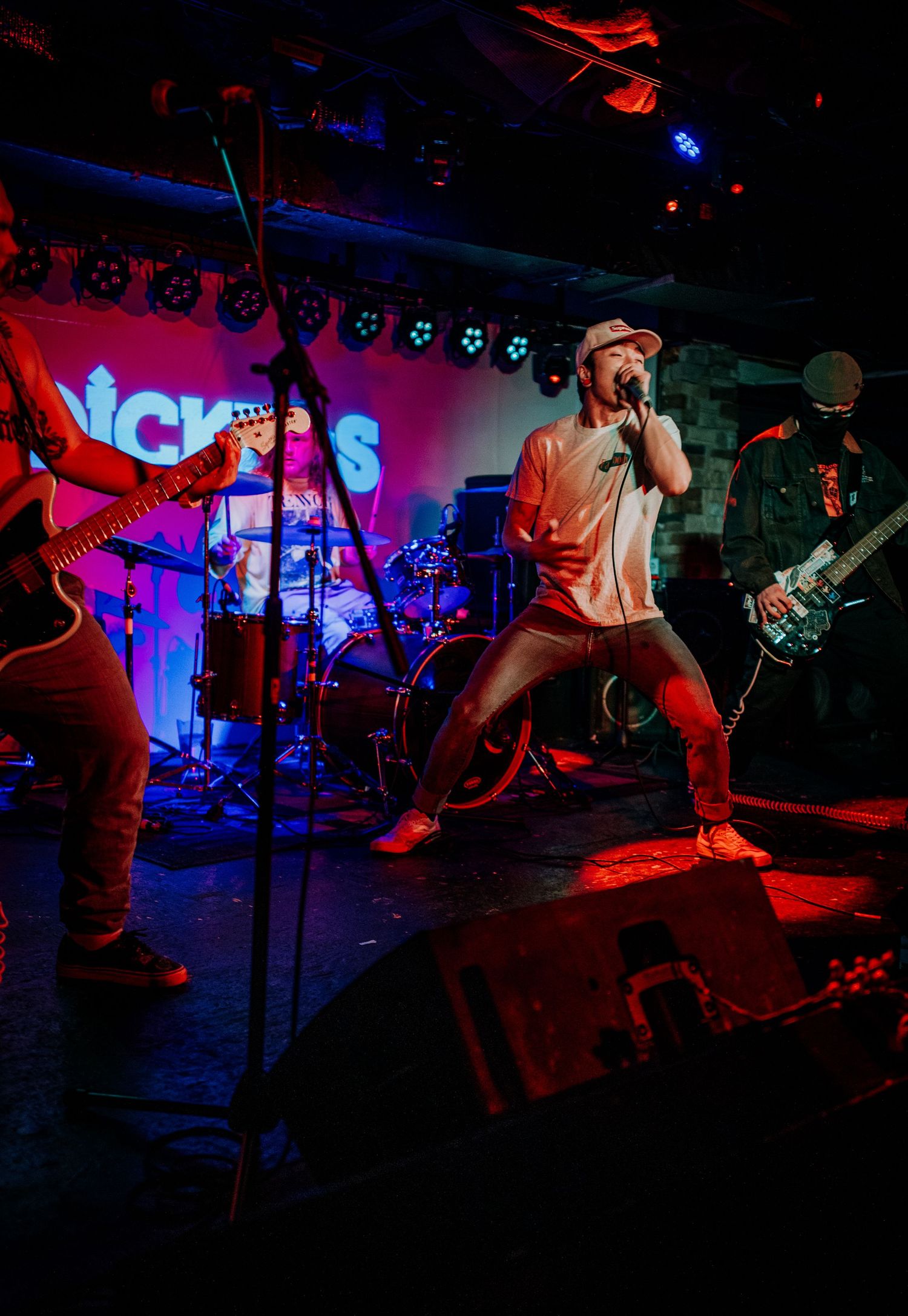 Performer on stage singing with band members in background under dramatic red and blue lighting.