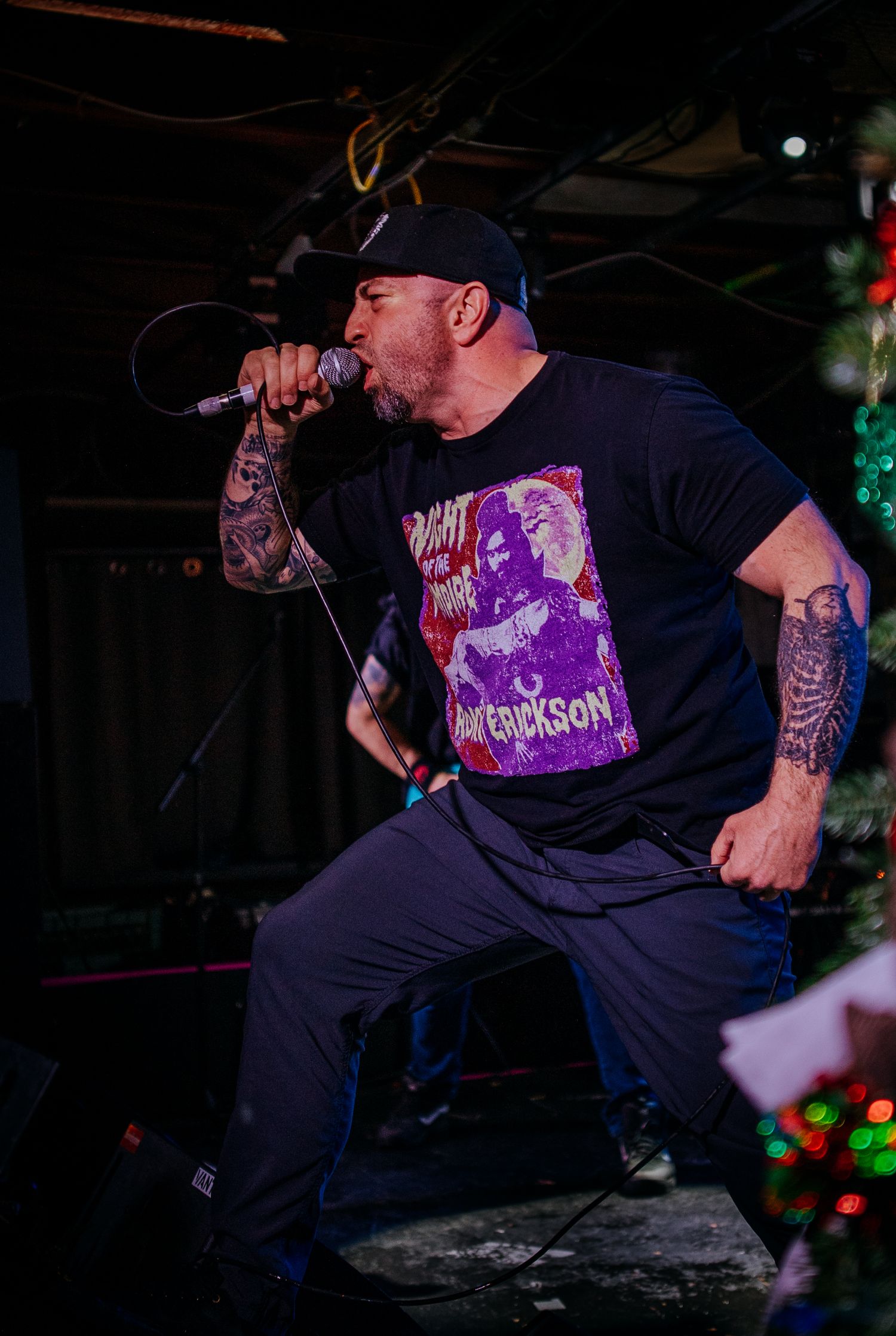 Tattooed vocalist performs passionately on stage wearing black t-shirt and baseball cap.