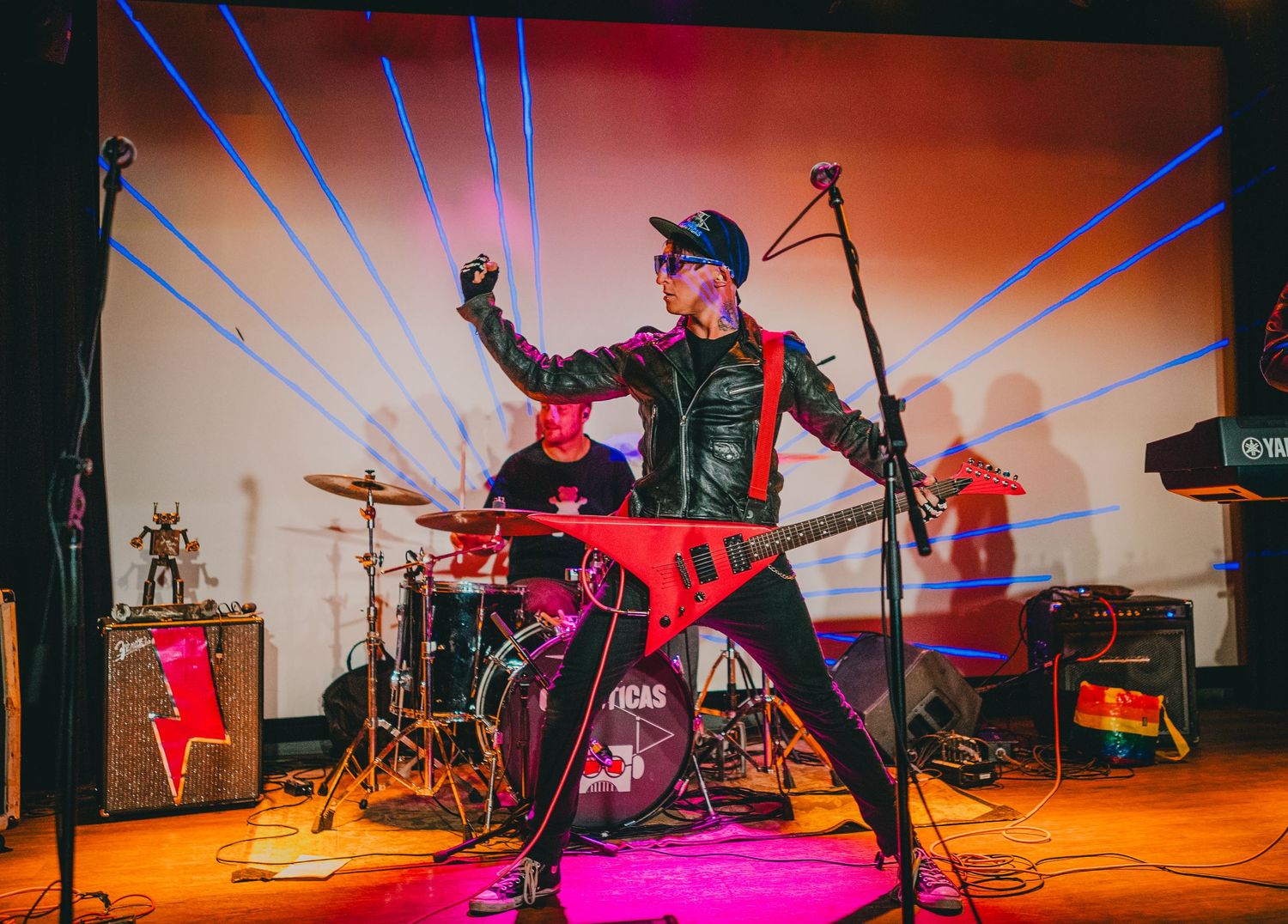 Dynamic performer in military-style jacket strikes pose on colorfully lit stage during live show.