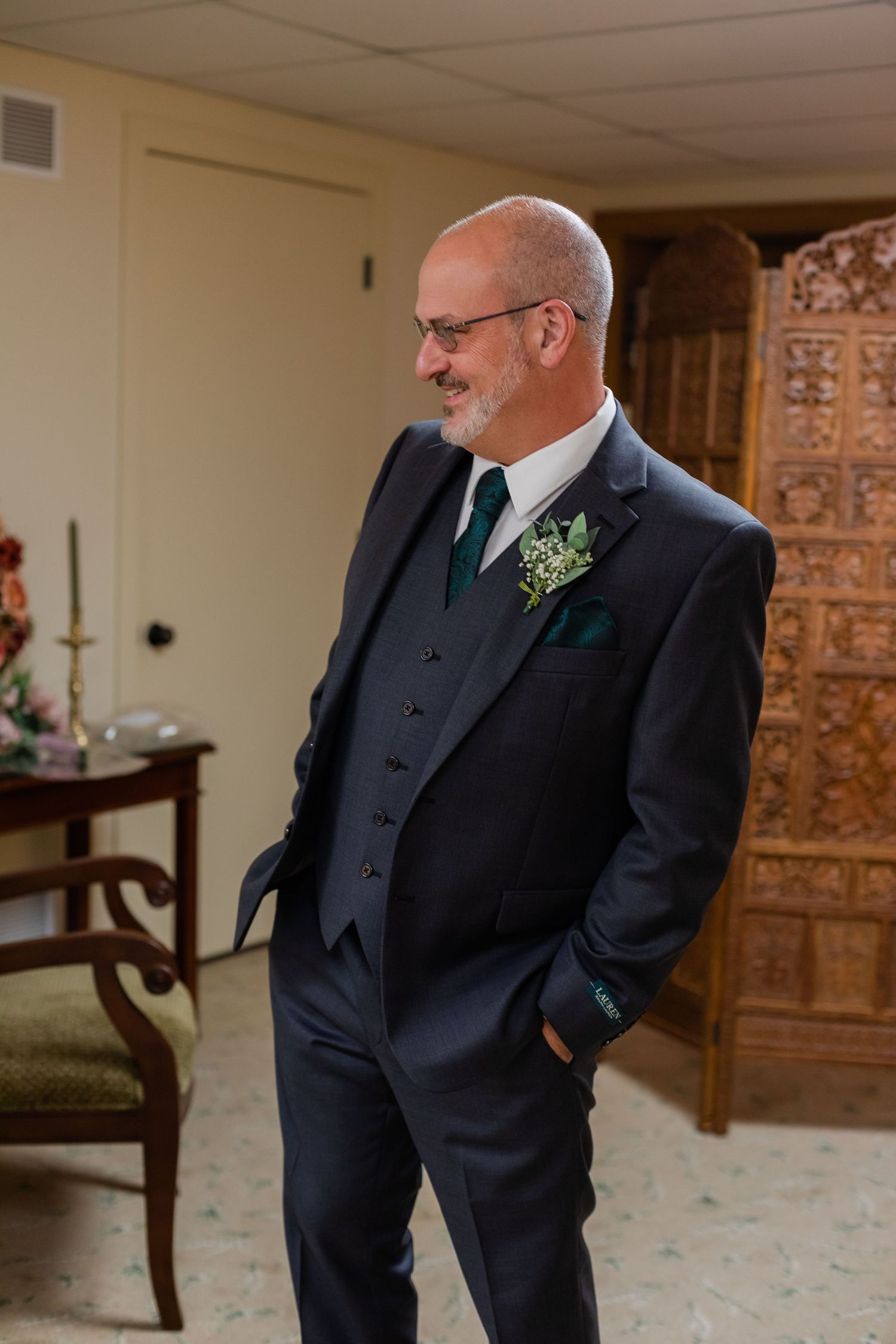 Groom in dark suit with boutonniere smiles while waiting.