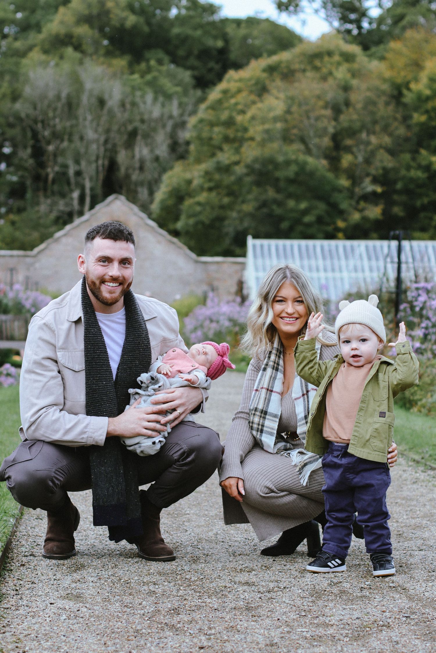 Family with young children posing together in front of lush garden greenery.