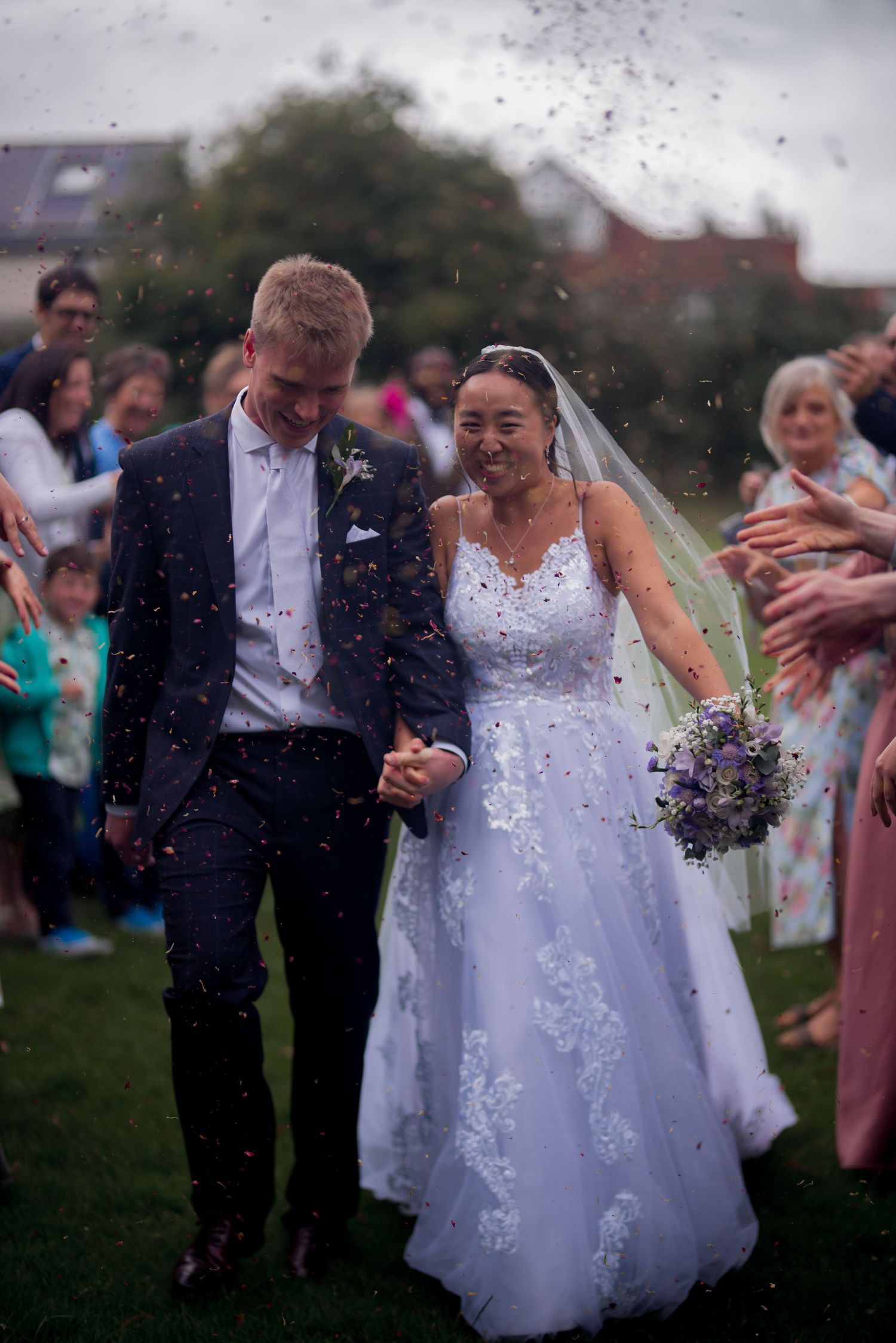A just-married bride and groom walking through a confetti tunnel outside