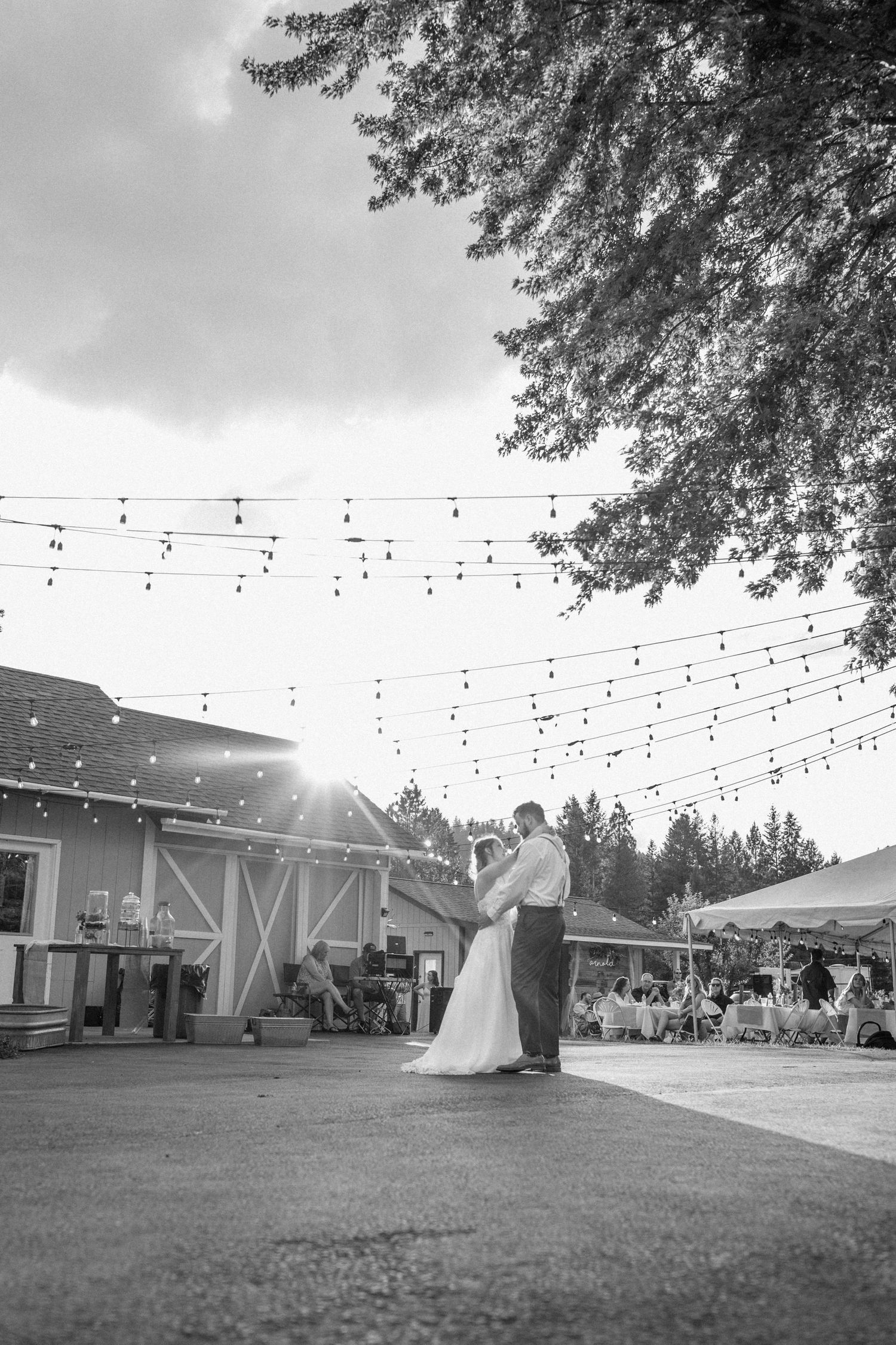 A couple shares their first dance at an outdoor wedding reception under string lights at sunset.