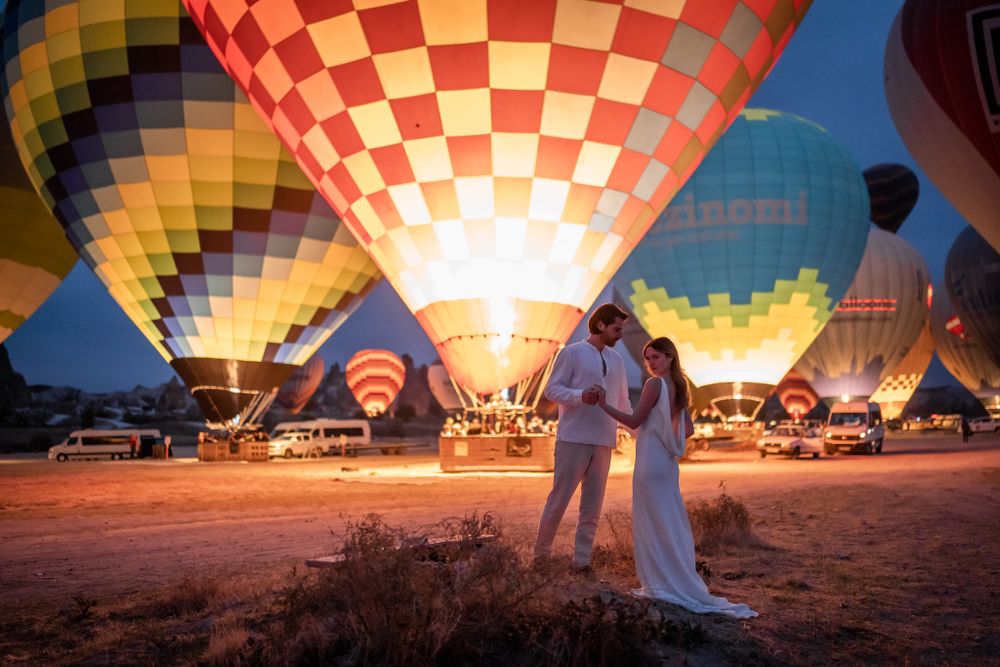 Silhouetted couple at hot air balloon festival with colorful glowing balloons at sunrise.