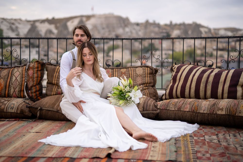 A couple resting on ornate cushions on a terrace overlooking a scenic landscape.