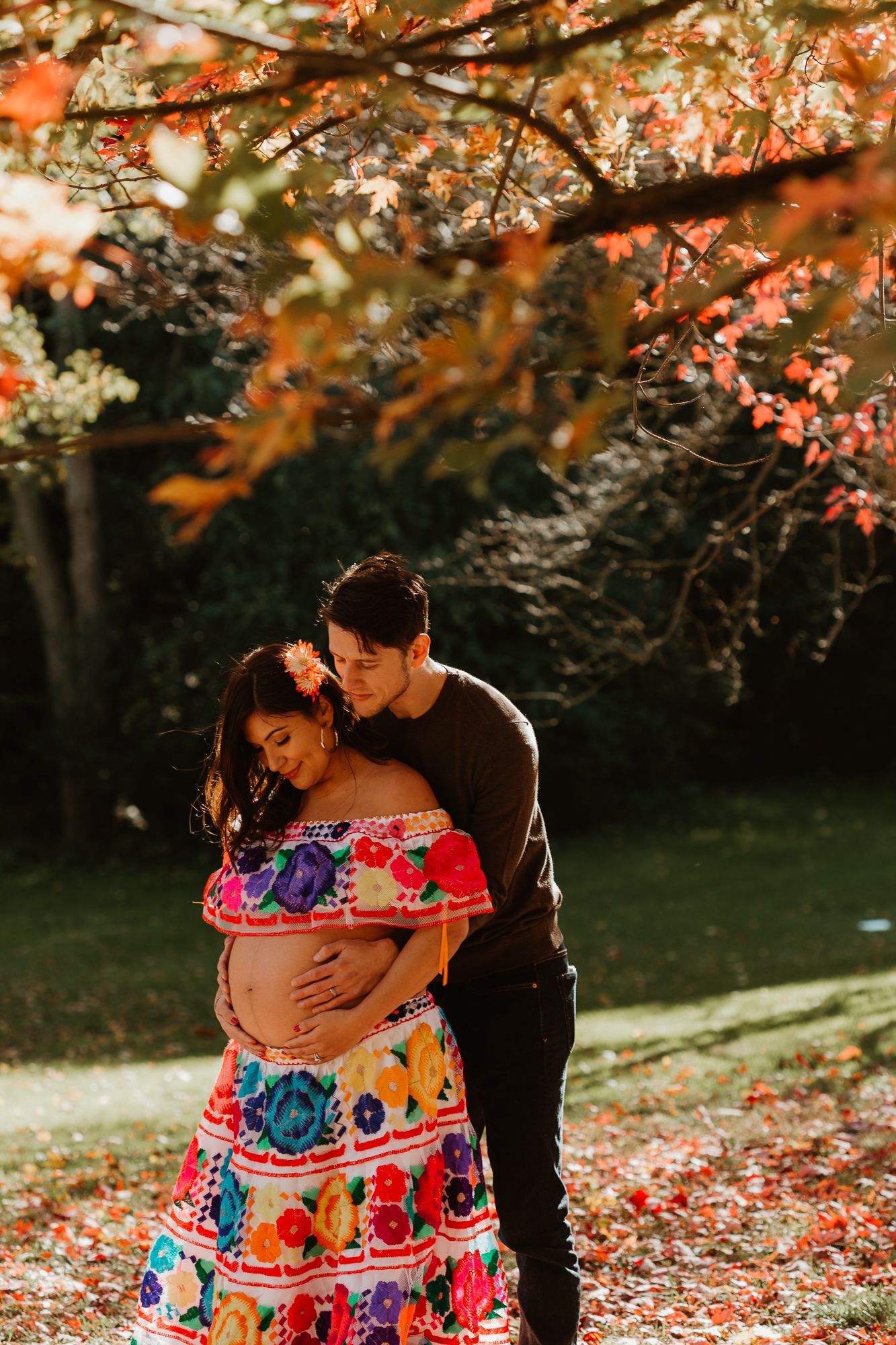 A couple shares an intimate moment under autumn trees with colorful foliage.