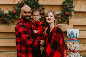 Family wearing coordinated buffalo plaid outfits poses by festive holiday decorations.