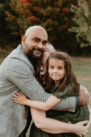 Family sharing a warm embrace during autumn photo session with fall foliage in background.