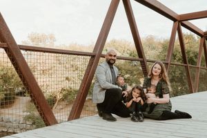 A family sits together with their dog on a rustic bridge.