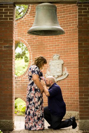 A proposal moment under a large bell with brick architecture backdrop.