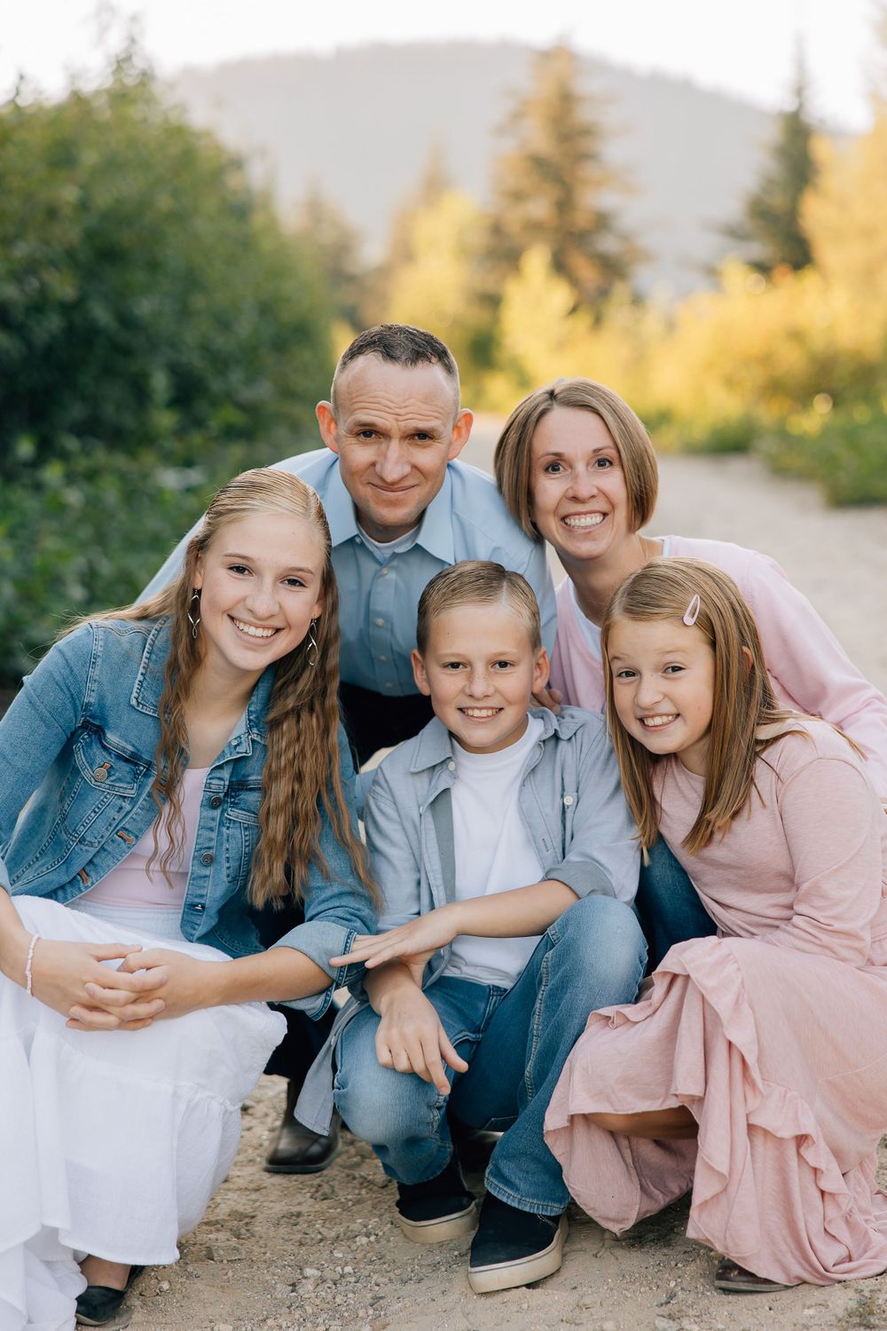 Portrait of a happy family sitting together outdoors with mountains and trees in the background.