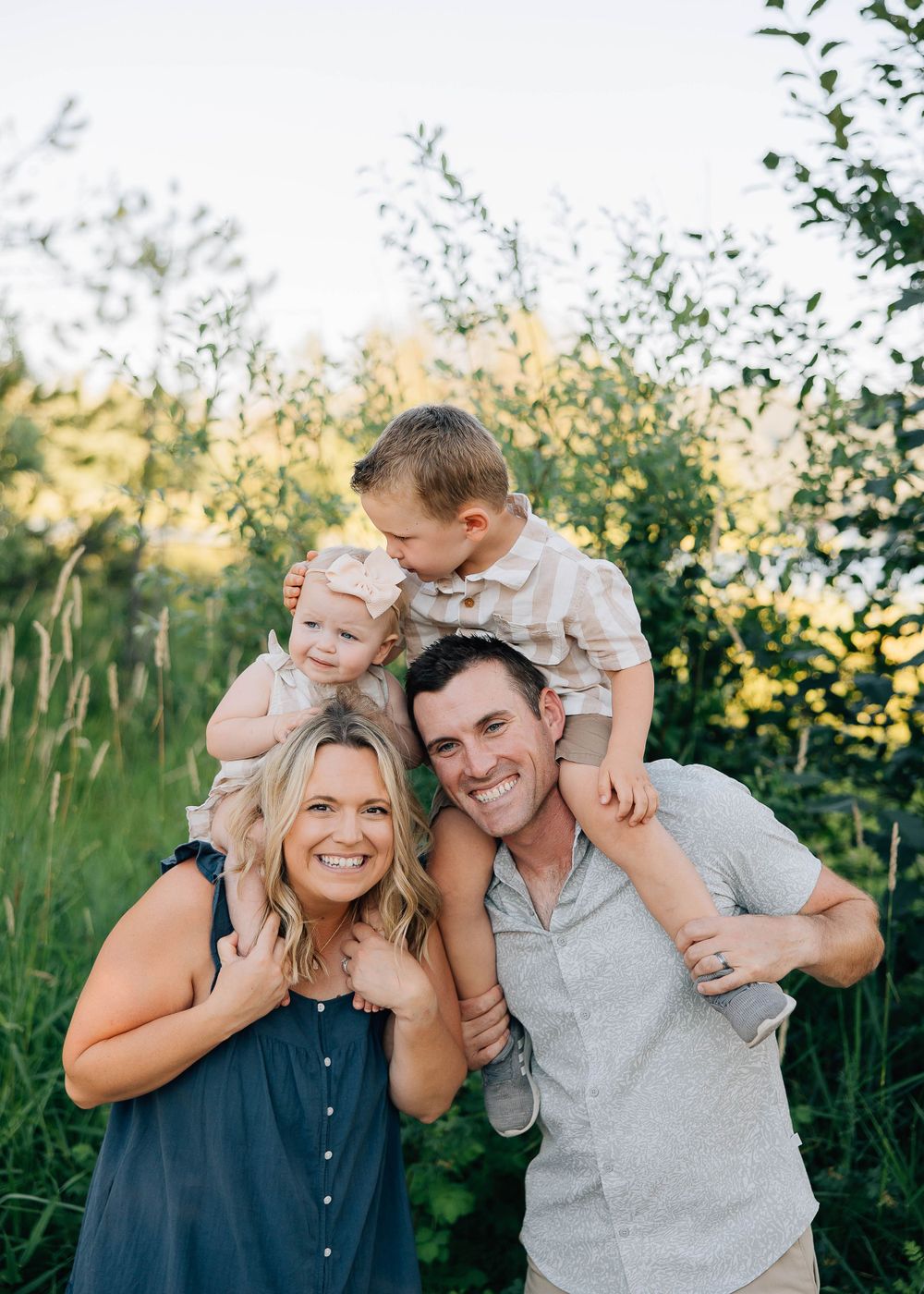 A loving family portrait outdoors with natural backlight and greenery during golden hour.