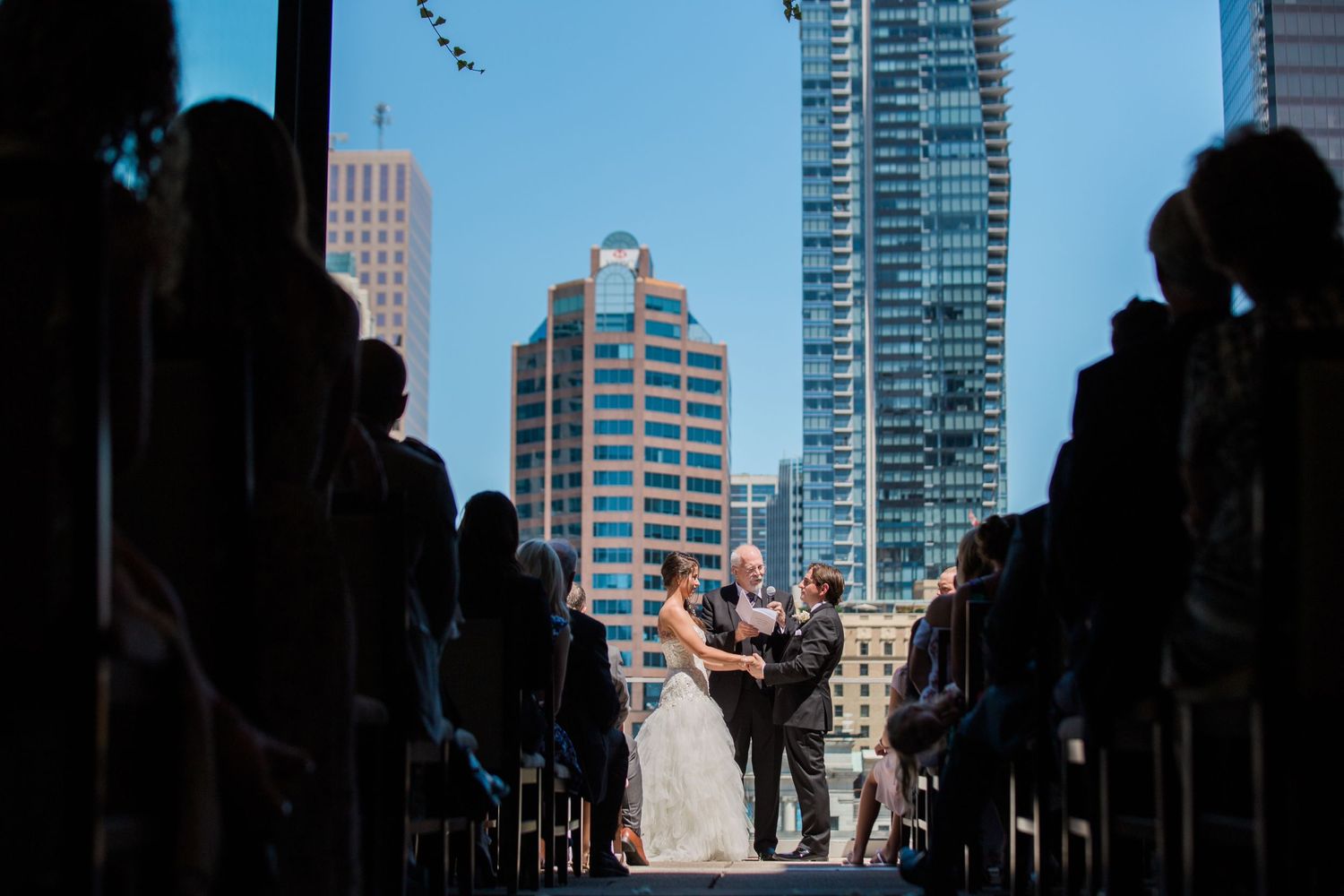 Ceremony taking place with city skyscrapers visible through large windows in background.