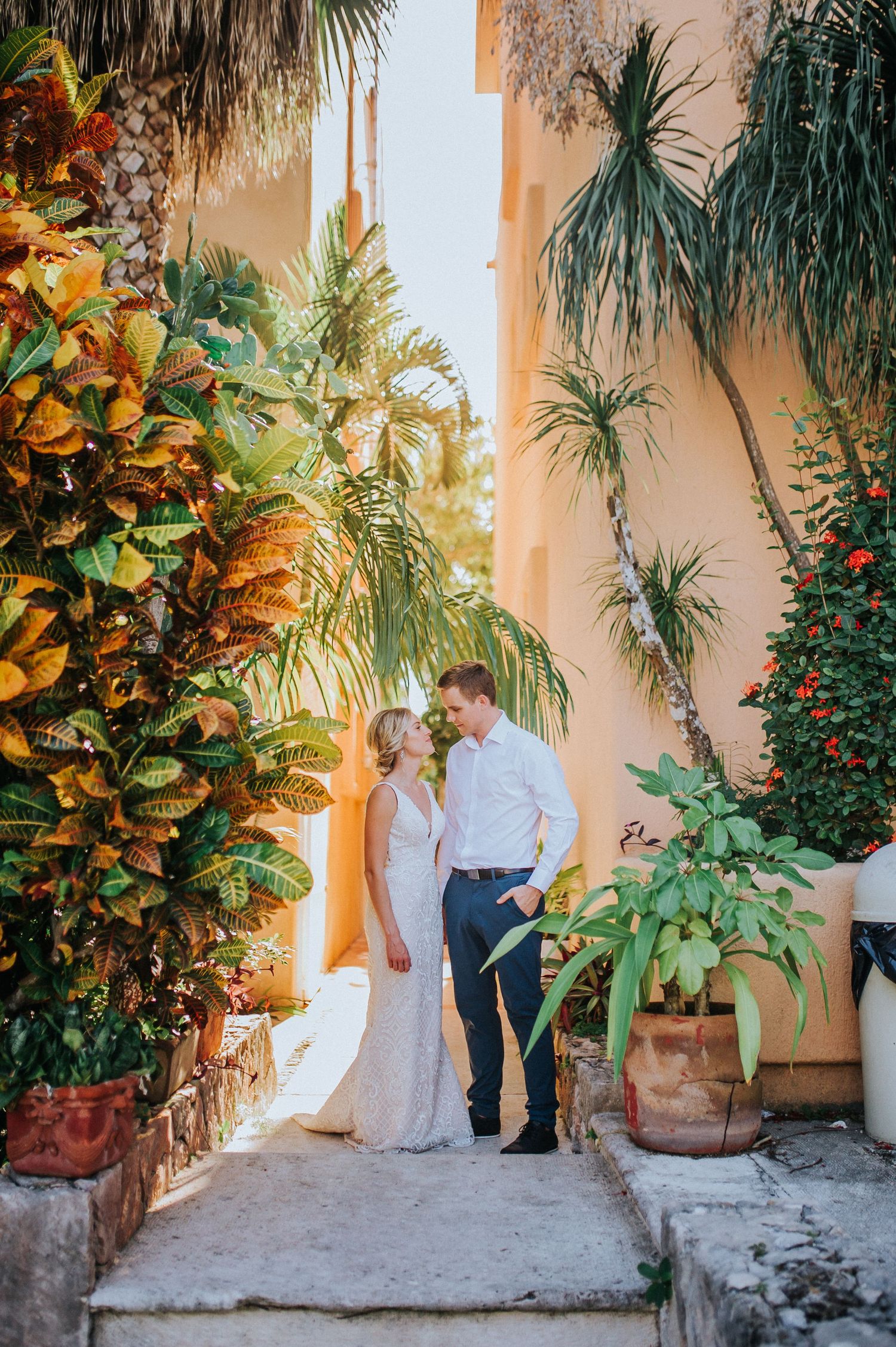 Couple in formal attire posing in tropical garden setting with lush foliage.