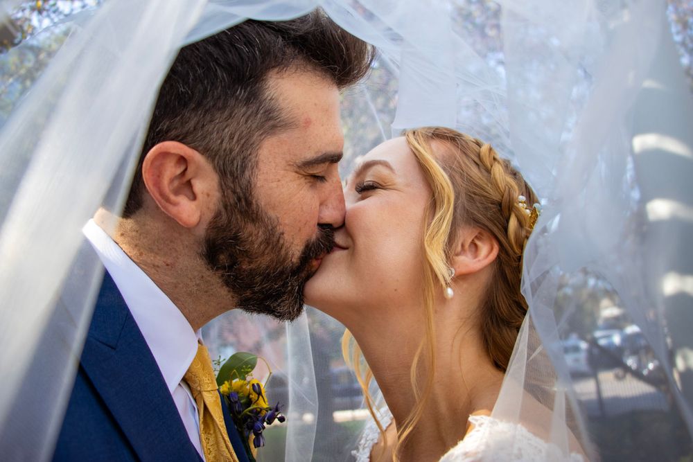 Romantic wedding kiss under a veil with delicate sunlight filtering through.