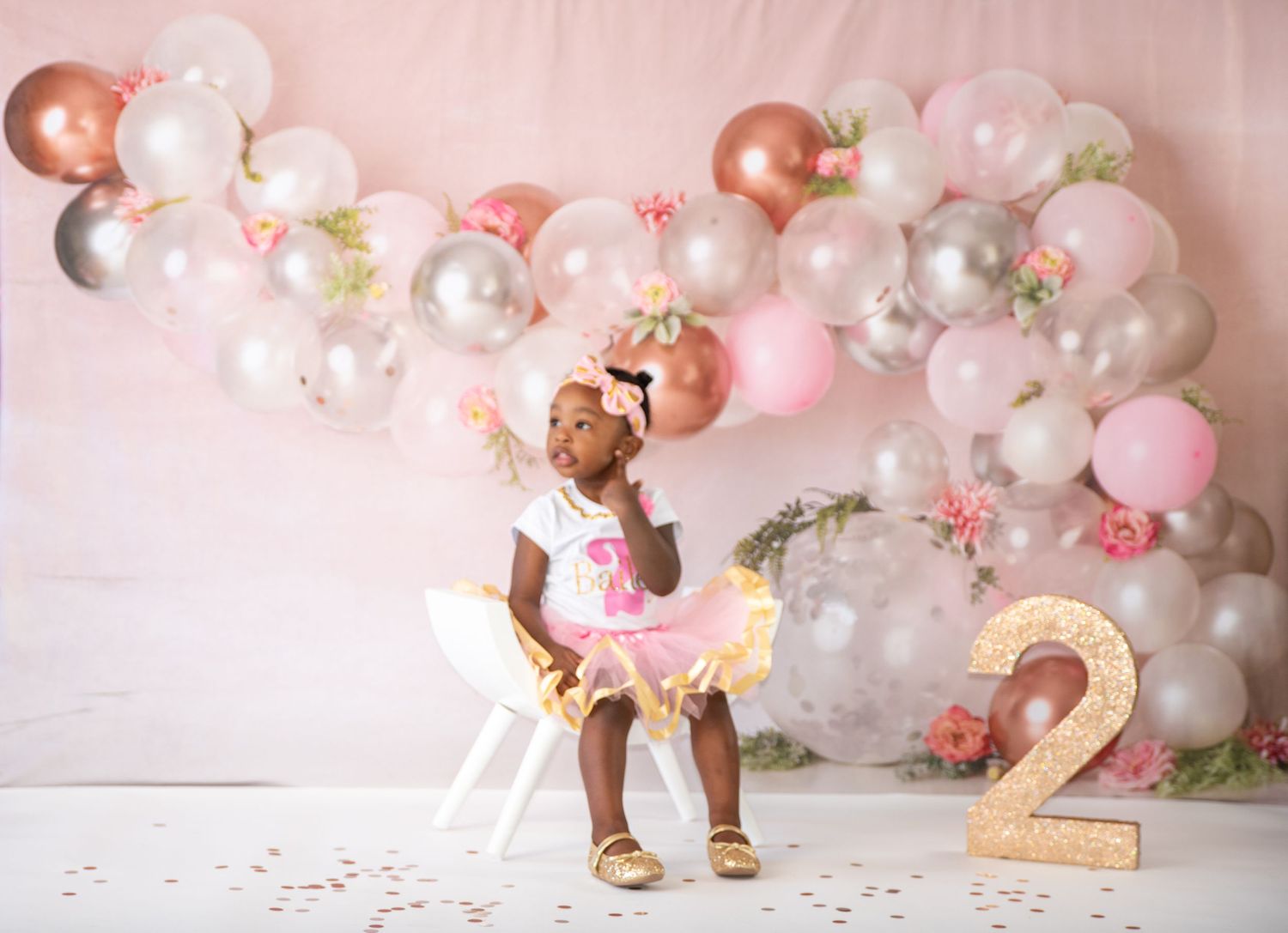 Pink and rose gold balloon arch decorates second birthday photoshoot setup.