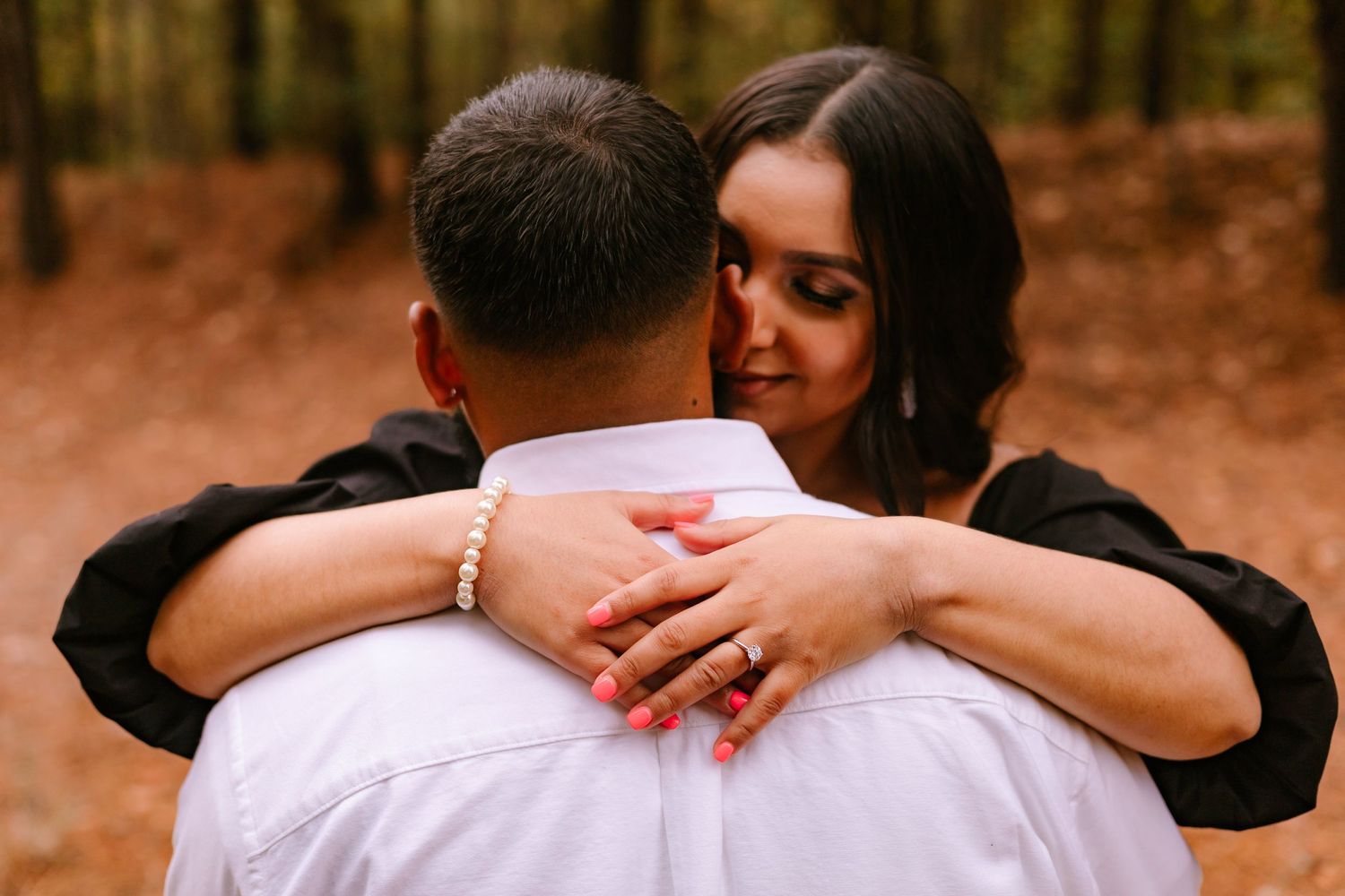 Woman with dark hair embracing man from behind in a warm autumn forest setting.