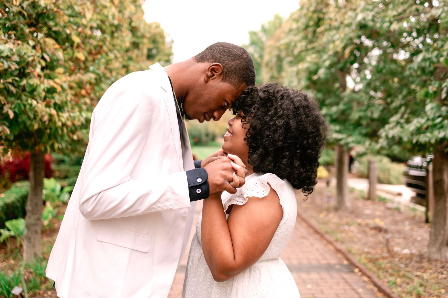 Black couple sharing a romantic forehead touch moment in a lush garden setting.