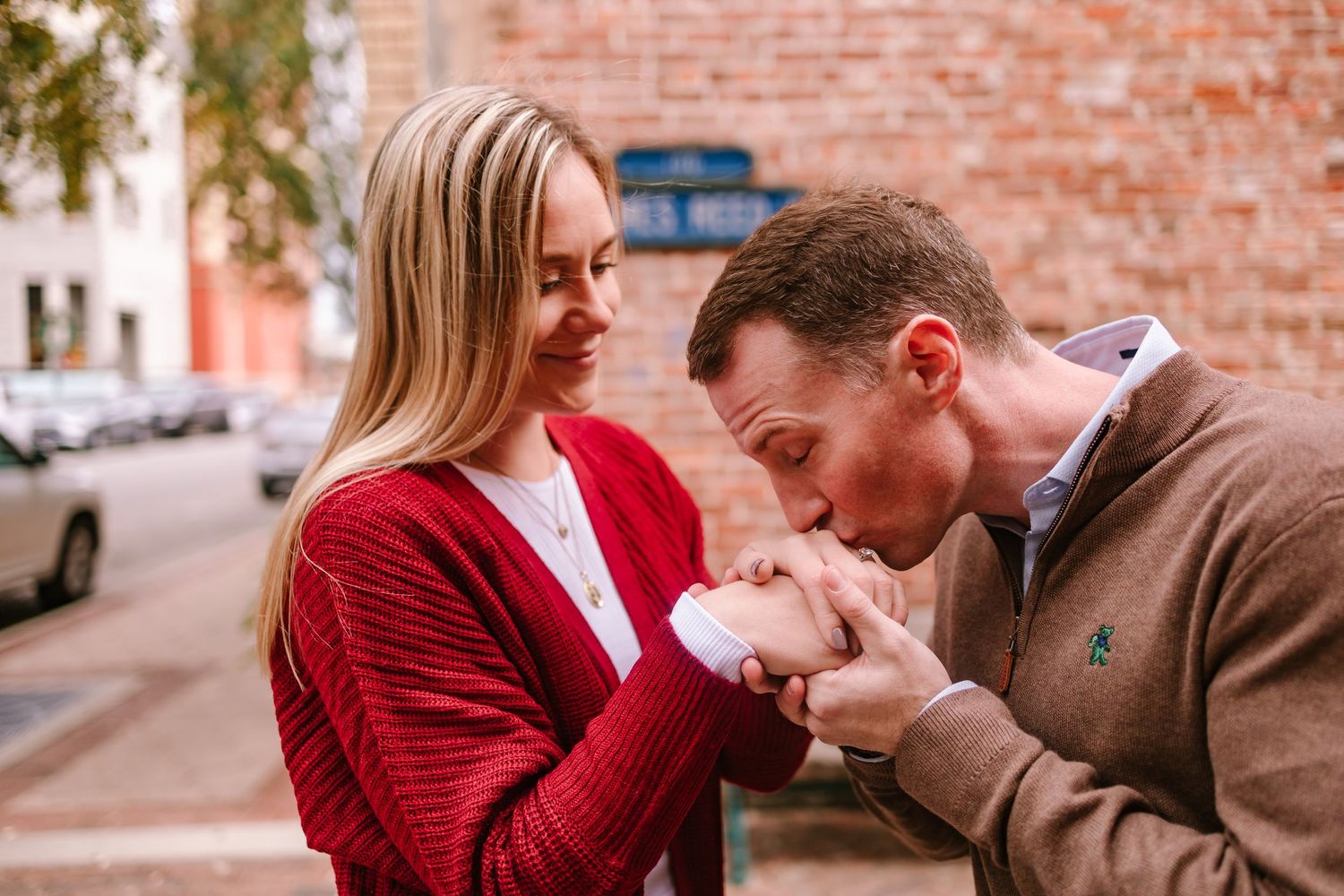 Man kissing woman's hand outdoors, couple sharing romantic moment on urban street.