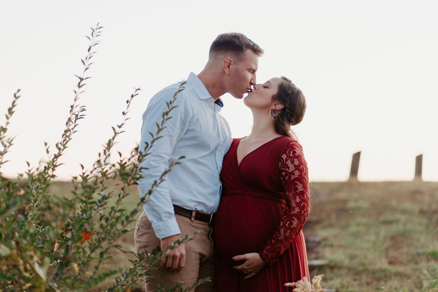 Expecting couple sharing a kiss in an open field during a fall maternity photo session.