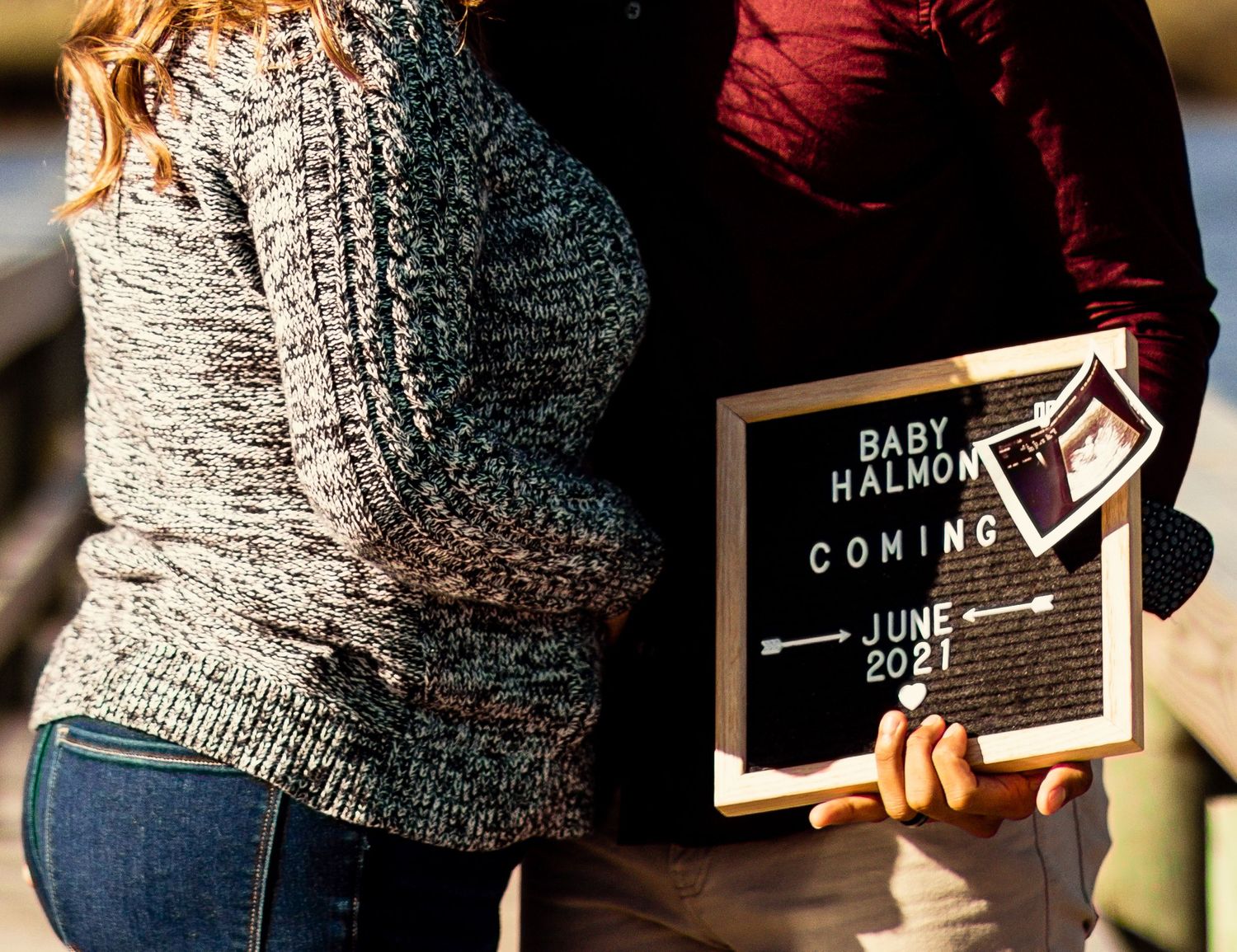 Couple holds a letter board pregnancy announcement sign reading Baby Halmon Coming June 2021.