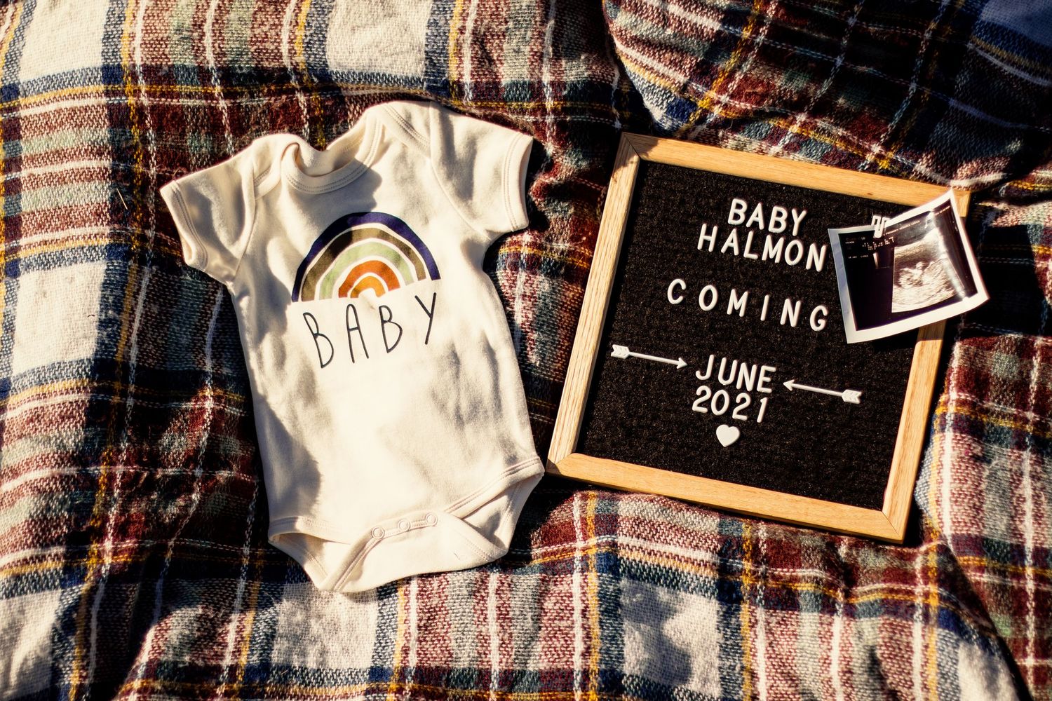 Baby announcement flat lay with onesie and letter board reading Baby Halmon Coming June 2021.