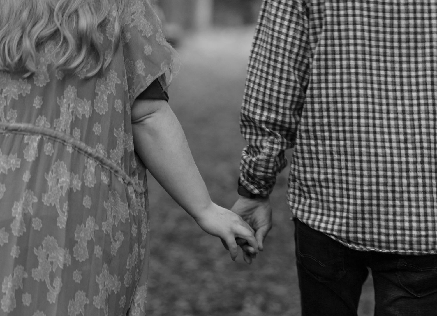 Black and white close-up of pregnant woman and partner holding hands tenderly during outdoor maternity shoot.