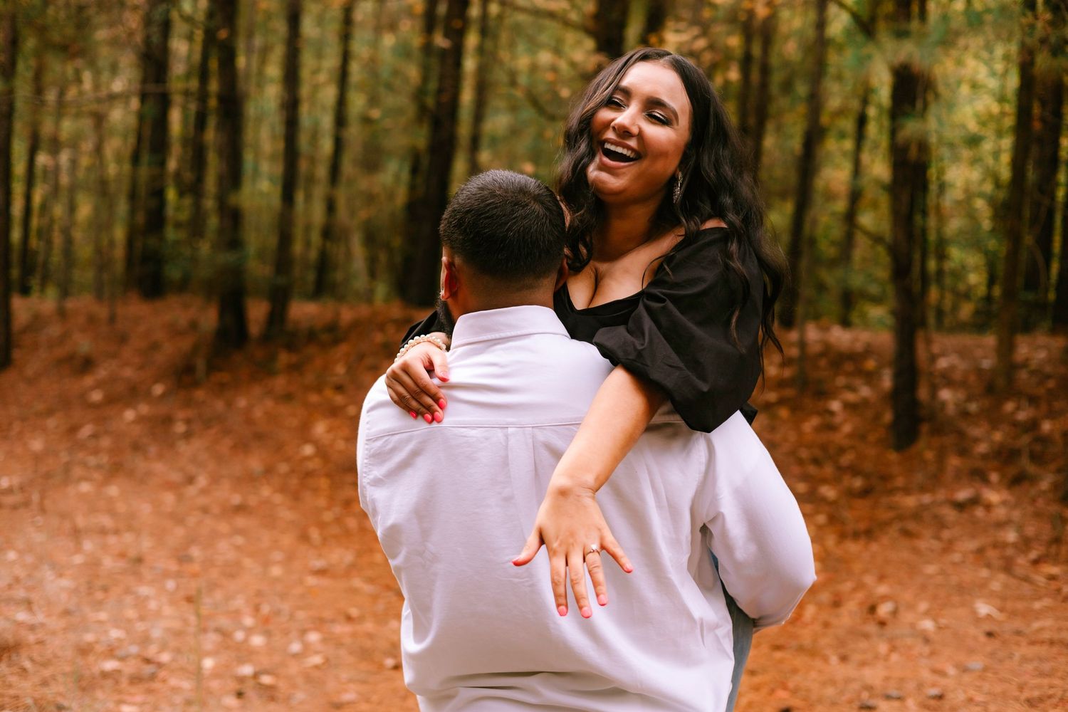 Man lifting and spinning laughing woman with long dark hair in an autumn forest.