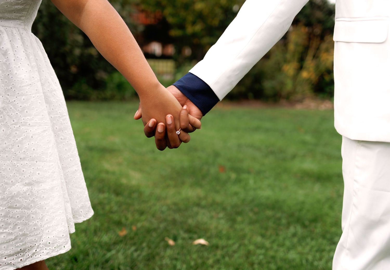 Close-up of an interracial couple holding hands on a green grass lawn outdoors.