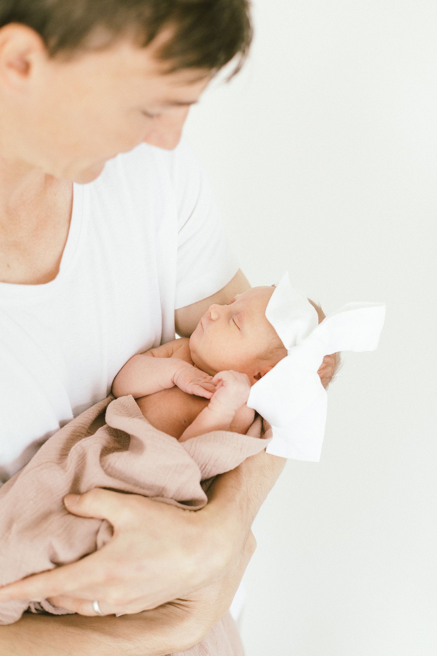 Tender close-up photos of parent cradling newborn baby in white setting.