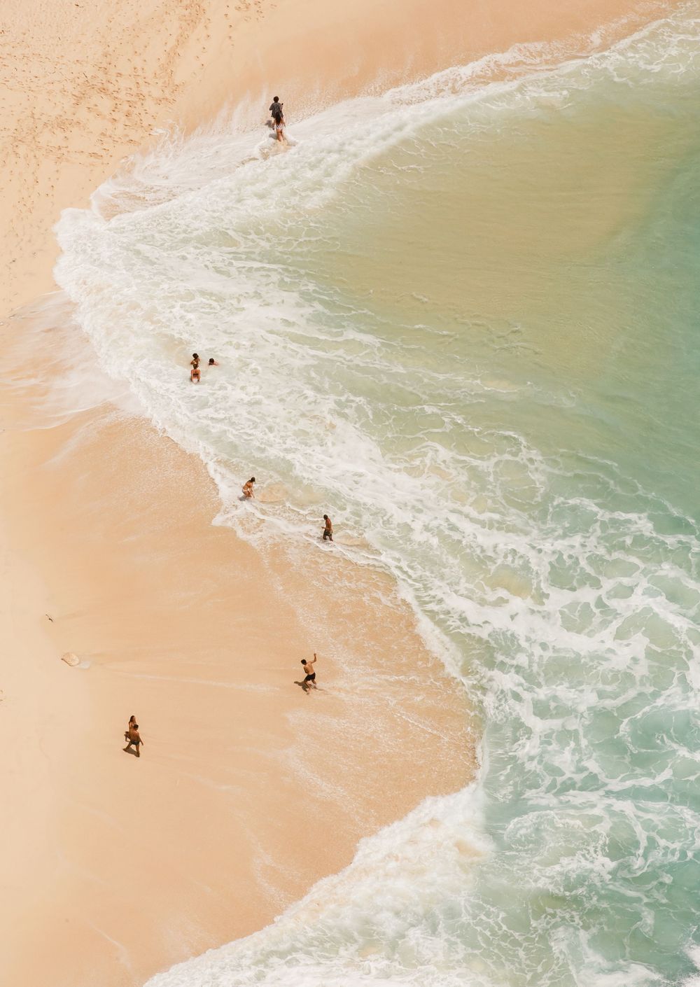 Aerial view of people spread along a sandy beach with turquoise waves washing ashore.