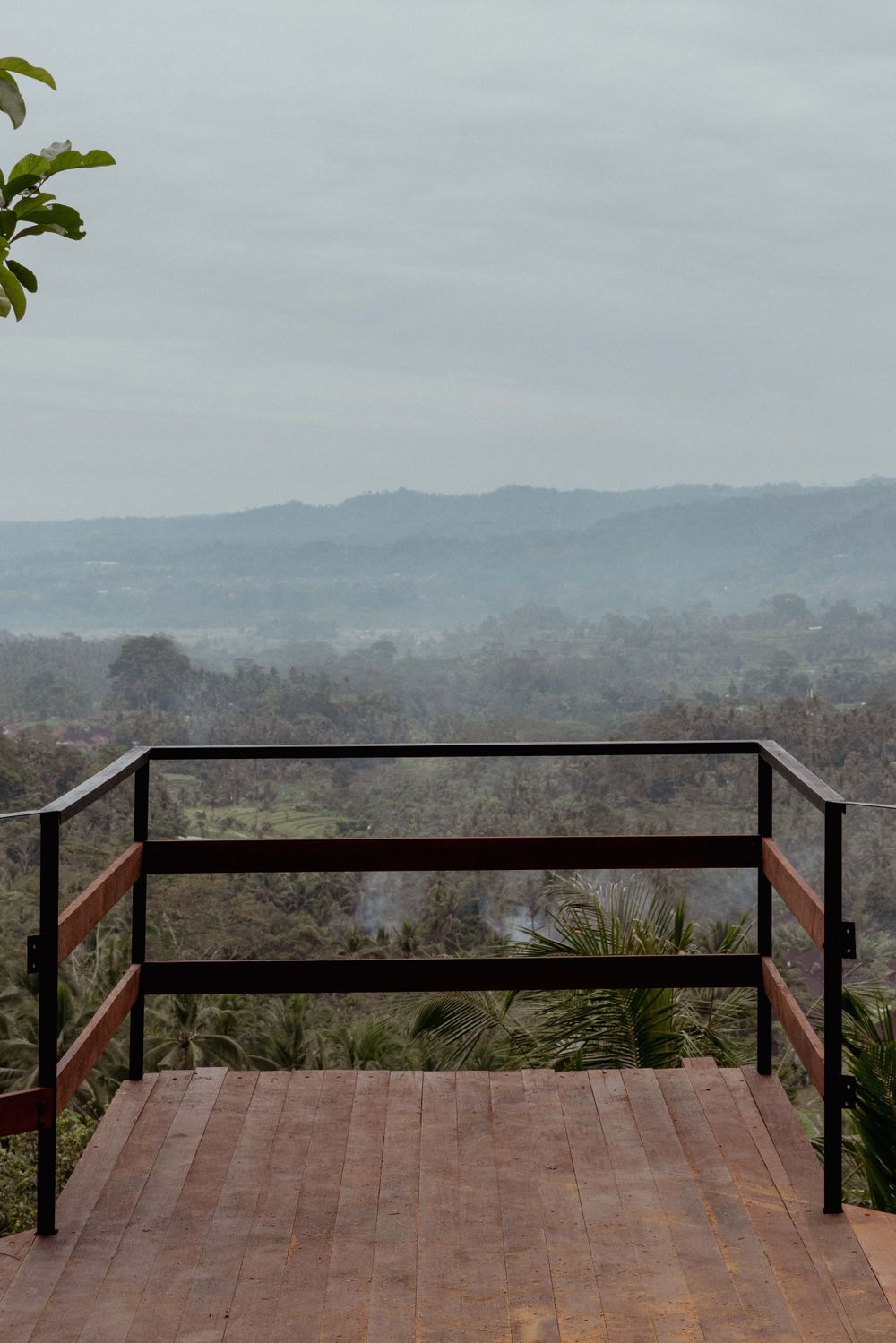 Wooden viewing platform with metal railings overlooking misty mountain landscape.