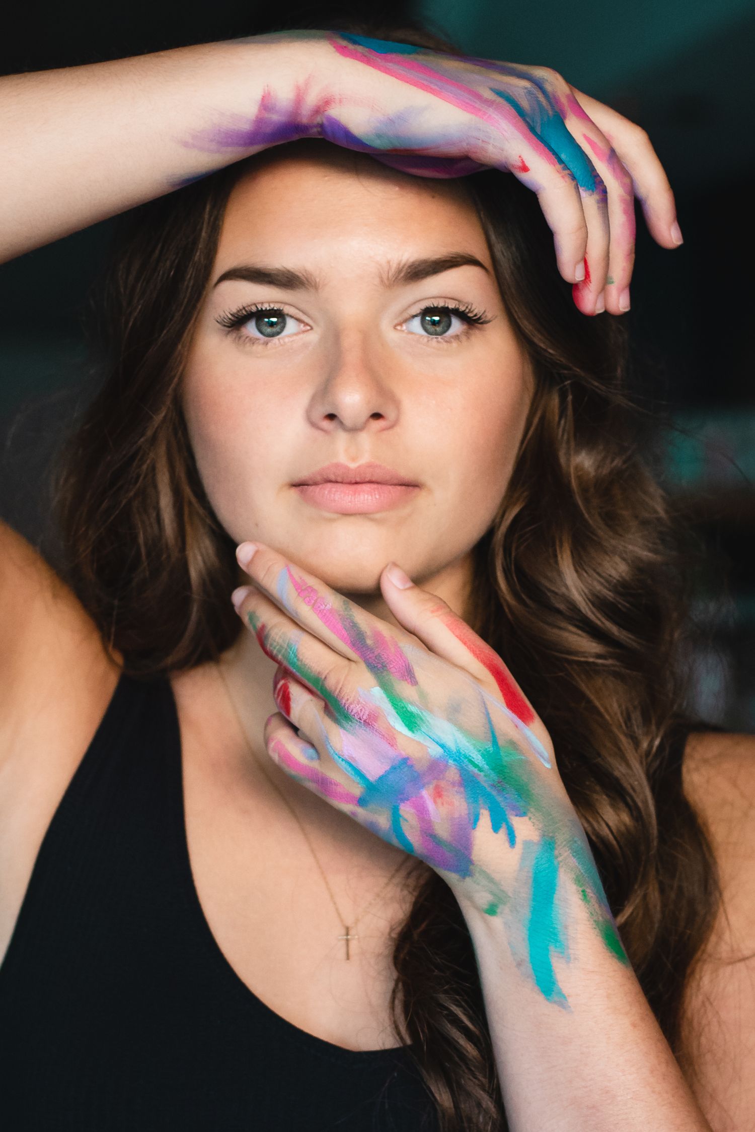 Artistic portrait with hands painted in vibrant blues and purples framing face.