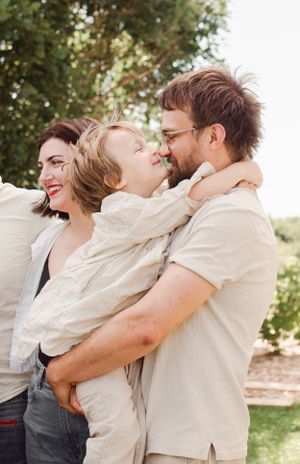 Tender moment of laughter and embrace between family members wearing light colored clothing outdoors.