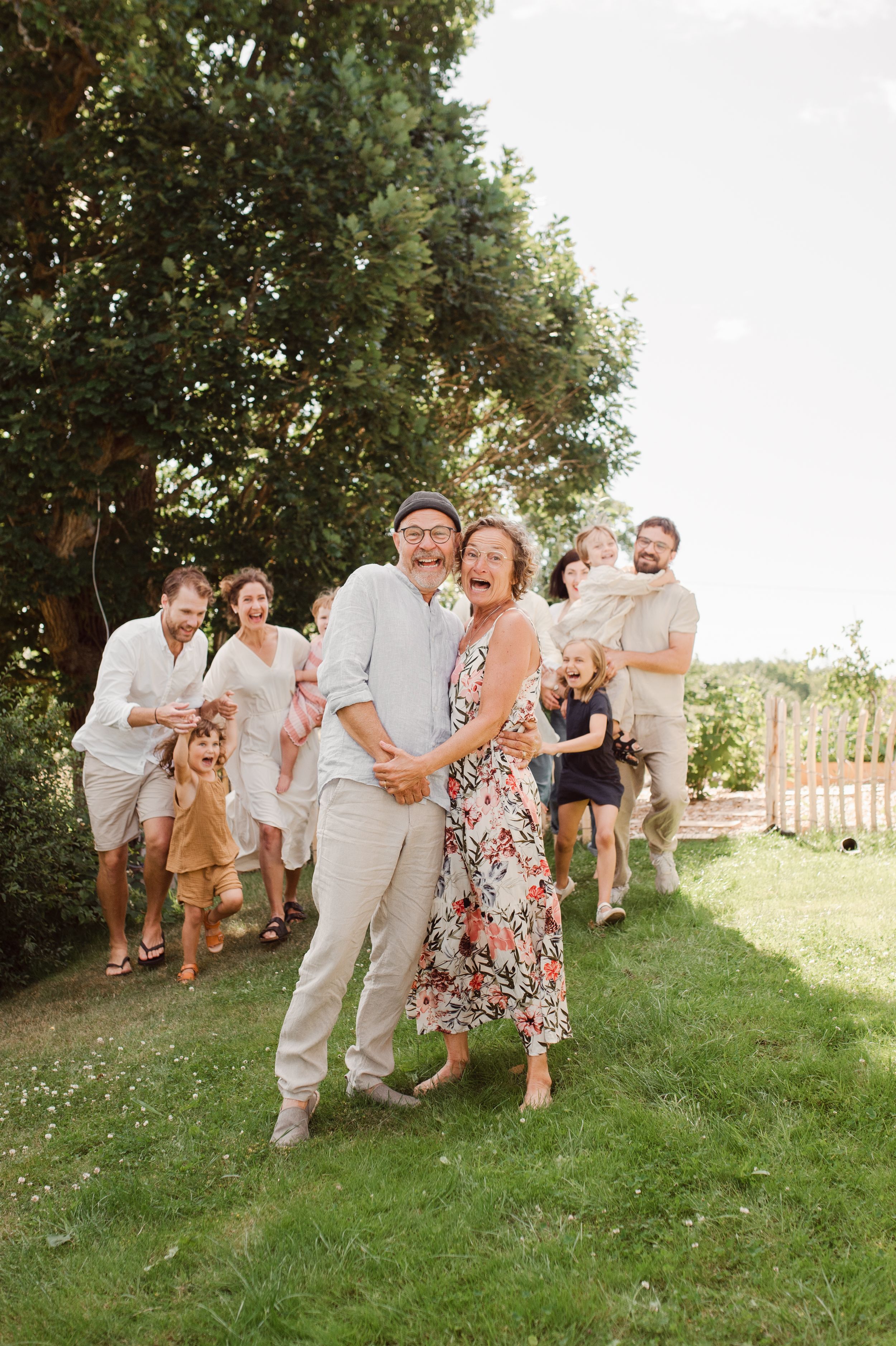 A group poses playfully for photos on a grassy lawn with trees in the background.
