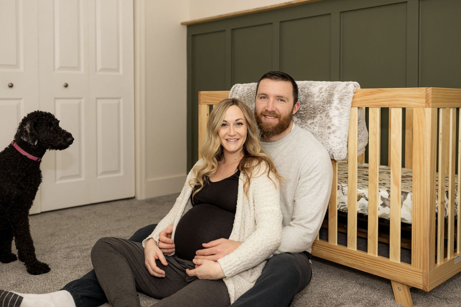 Candid family moment captured with couple and black dog by wooden furniture.