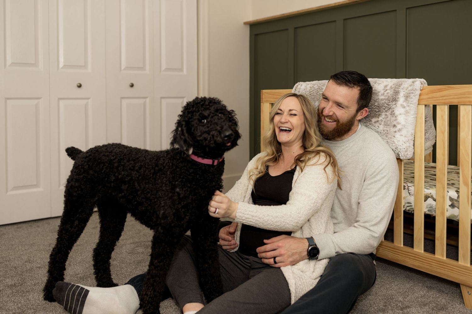 Intimate indoor photo session with couple and their black dog on carpeted floor.