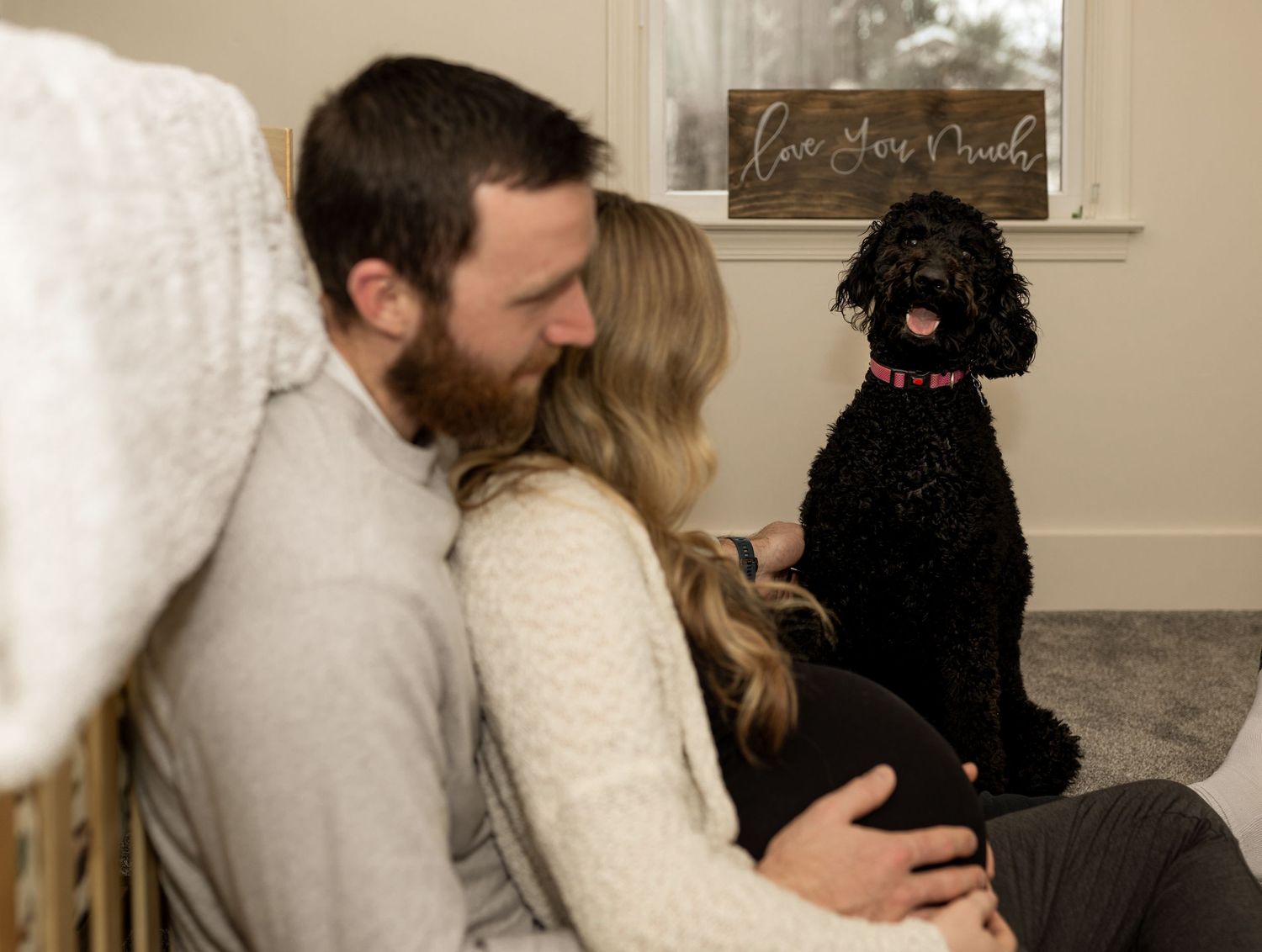 Black dog sitting with couple on carpeted floor in cozy nursery room.