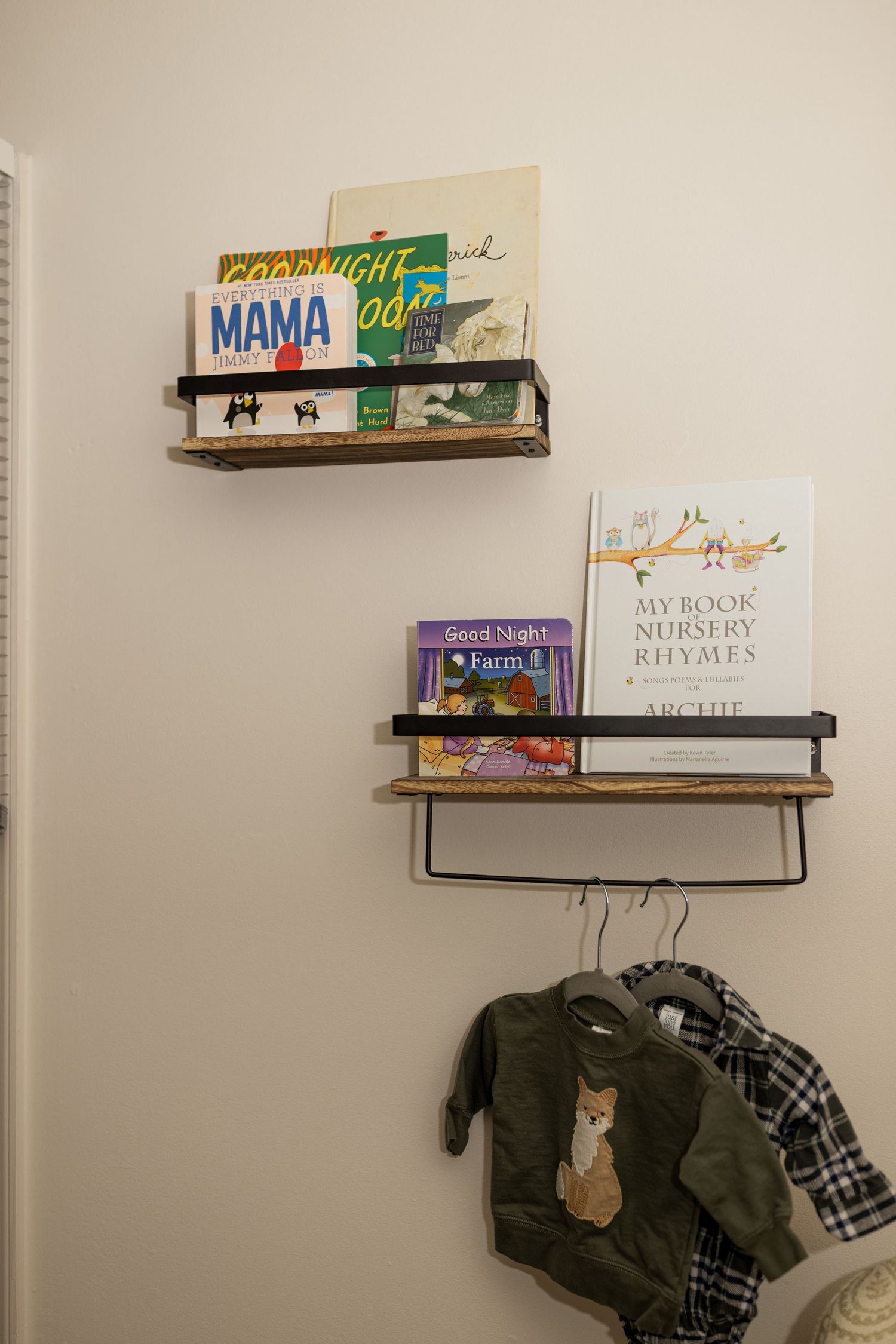 Floating wood and metal bookshelves displaying children's books against a beige wall.