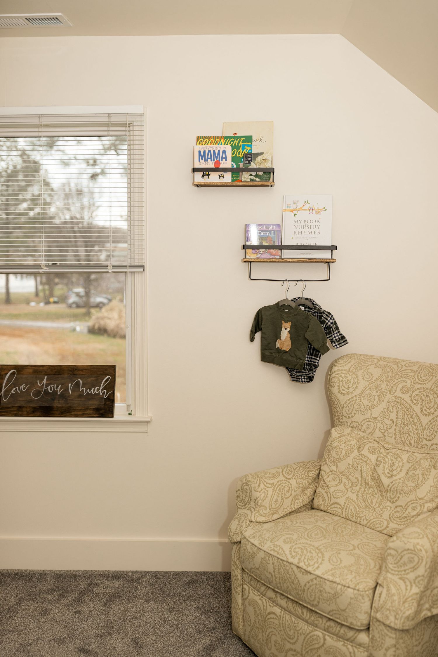 A comfortable reading nook with a patterned armchair and mounted bookshelves near a window.
