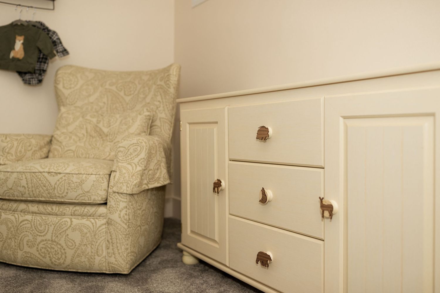 White built-in storage drawers beneath a cream-colored upholstered chair in a nursery setting.