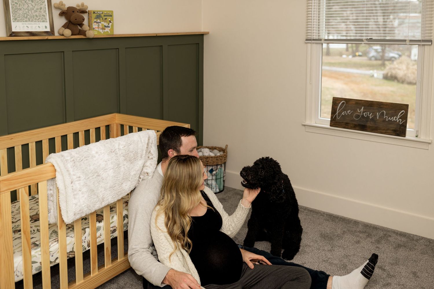 Family moment in nursery room with wooden crib and green accent wall.