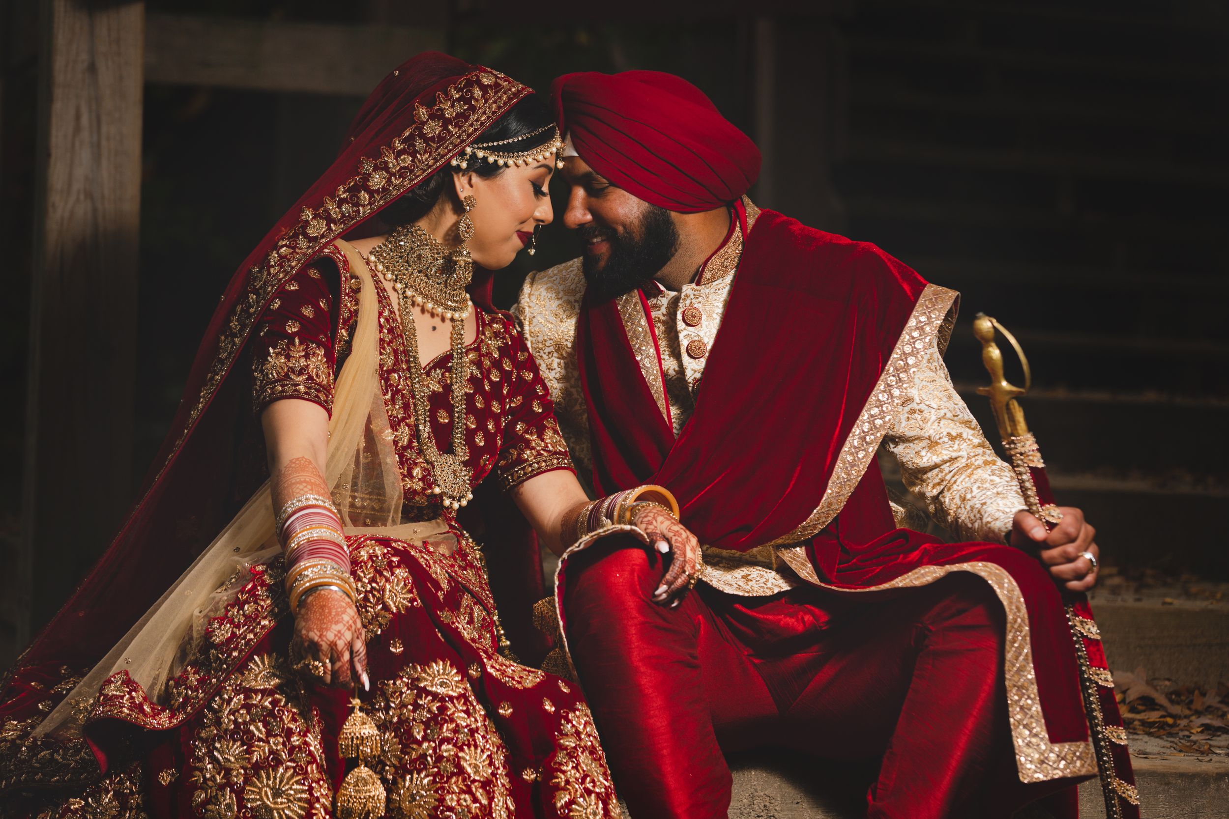 Intimate wedding couple in traditional red and gold Indian attire sharing a romantic moment together.