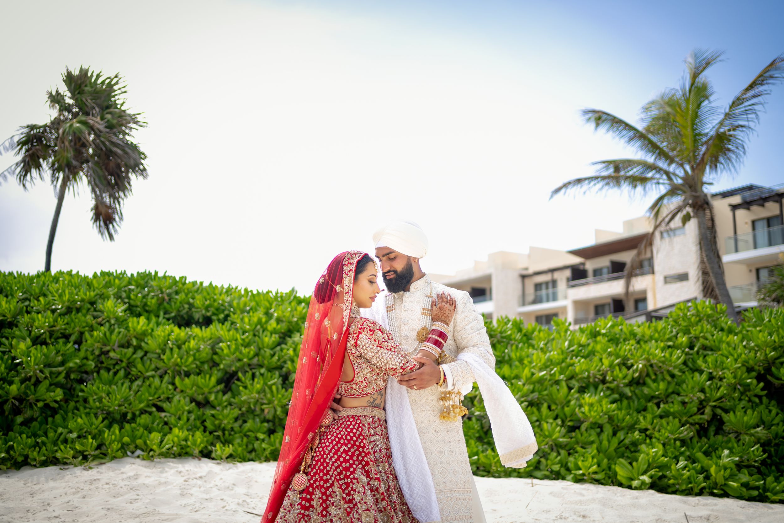 Traditional Indian wedding couple embraces on tropical beach with palm trees.
