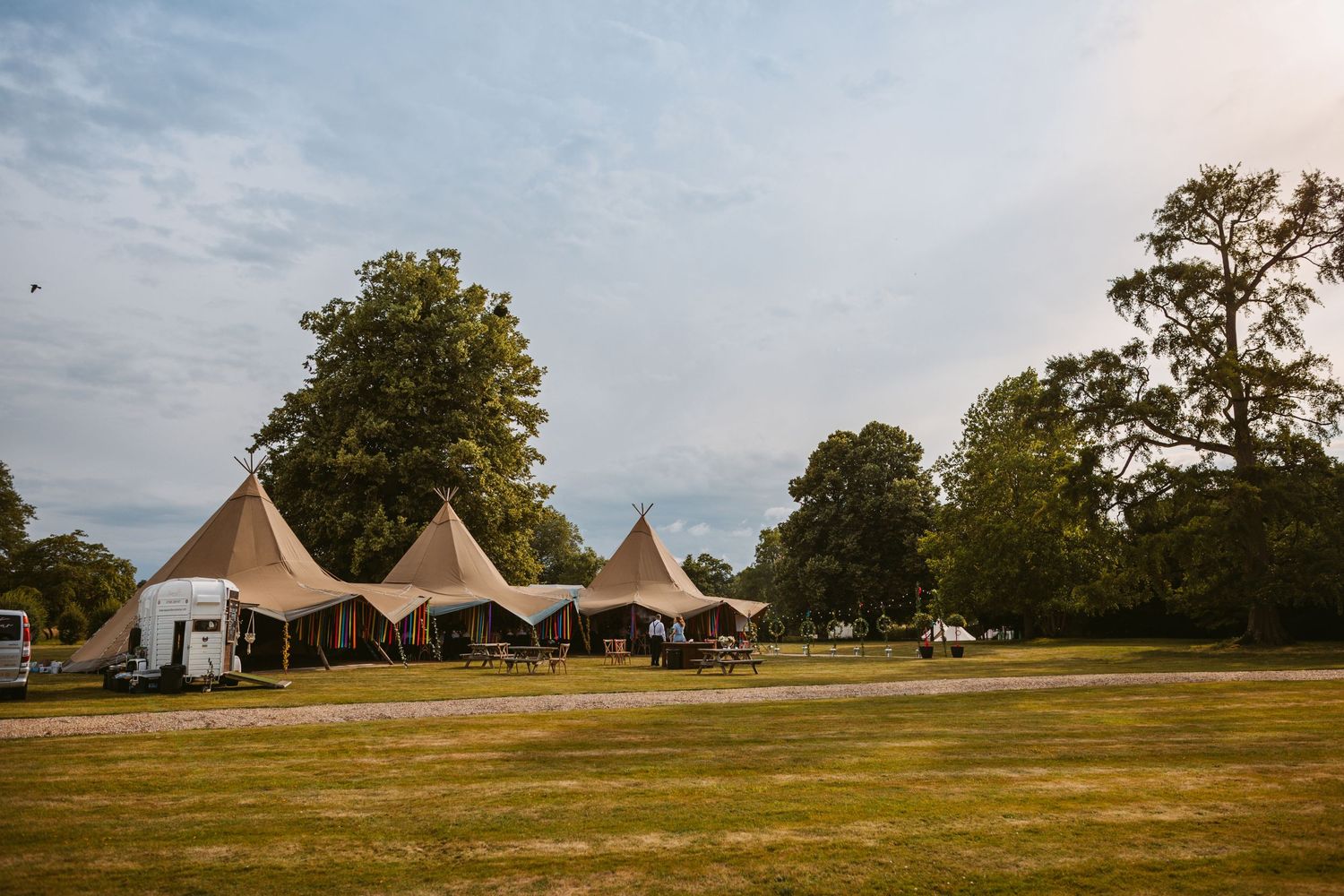 Tipi-style wedding reception tents set up on a spacious lawn during golden hour.